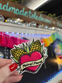 Load image into Gallery viewer, A sticker with a design featuring a heart and the text 'Midwest Princess', with decorative elements resembling corn and knobs.
